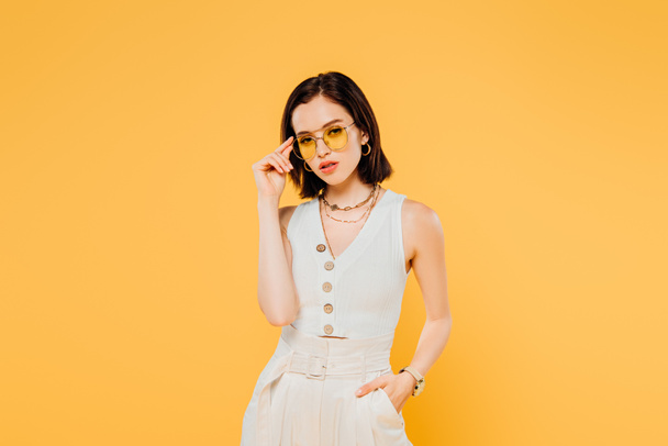 stylish woman in sunglasses posing with hand in pocket isolated on yellow - Photo, Image