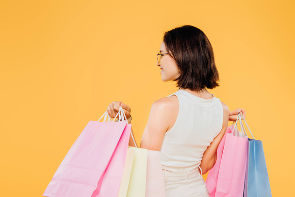 back view of woman in sunglasses holding shopping bags isolated on yellow - Photo, image