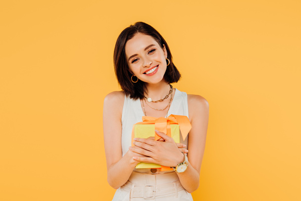Gelukkig glimlachend meisje Holding Gift Box geïsoleerd op geel - Foto, afbeelding