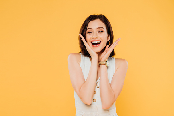 excited smiling elegant girl with hands near face isolated on yellow - Foto, Imagem