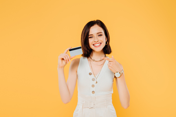 smiling elegant girl pointing with finger at credit card isolated on yellow - Fotografie, Obrázek