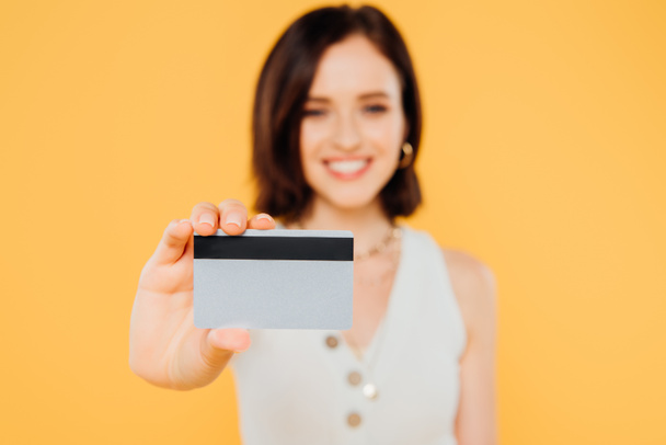 selective focus of smiling elegant girl holding credit card isolated on yellow - Fotoğraf, Görsel