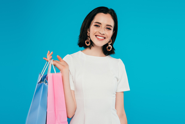 mujer elegante sonriente en vestido con bolsas de compras aisladas en azul
 - Foto, imagen