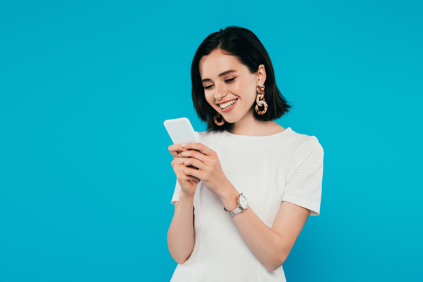 smiling elegant woman in dress using smartphone isolated on blue - Photo, Image