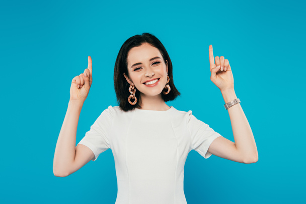 smiling elegant woman in dress pointing with fingers upwards isolated on blue - Foto, Imagen