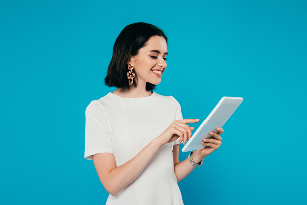 smiling elegant woman in dress using digital tablet isolated on blue - 写真・画像