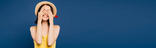 smiling girl in straw hat with hands on eyes isolated on blue - Foto, imagen
