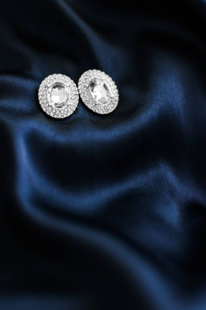 ダークブルーシルクの背景に豪華なダイヤモンドのイヤリング、ホリデーgl - 写真・画像