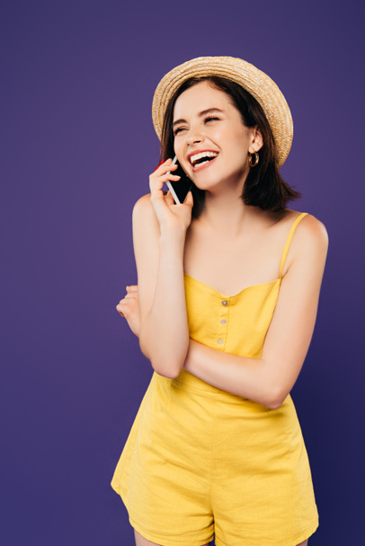 happy girl in straw hat talking on smartphone and laughing isolated on purple - Fotó, kép
