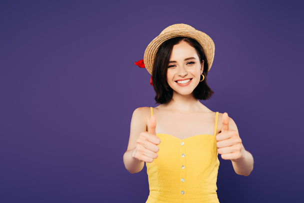 glimlachend mooi meisje in stro hoed tonen thumbs up geïsoleerd op paars - Foto, afbeelding