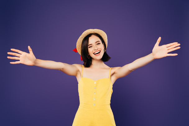 uśmiechnięta Ładna dziewczyna w słomkowym kapeluszu z otwartymi ramionami na fioletowym - Zdjęcie, obraz