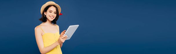 tiro panorâmico de menina bonita sorridente em chapéu de palha segurando tablet digital isolado em azul
 - Foto, Imagem