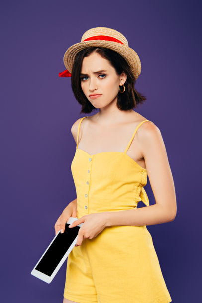 triste chica bonita en sombrero de paja celebración tableta digital con pantalla en blanco aislado en púrpura
 - Foto, Imagen