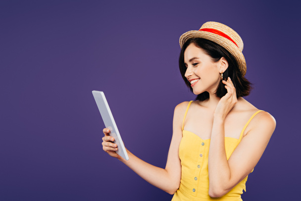 smiling pretty girl in straw hat holding digital tablet isolated on purple - Fotó, kép
