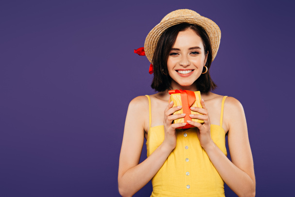 glimlachend meisje in stro hoed bezit aanwezig geïsoleerd op paars - Foto, afbeelding