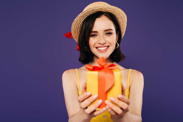 χαμογελαστή κορίτσι σε ψάθινο καπέλο δώρο δώρου που απομονώνεται σε μωβ - Φωτογραφία, εικόνα