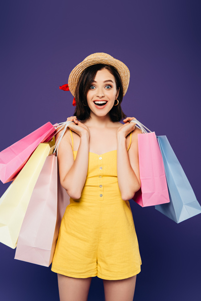 excited smiling girl in straw hat with shopping bags isolated on purple - Fotoğraf, Görsel