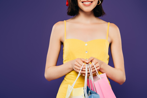 partial view of smiling girl in straw hat with shopping bags isolated on purple - Photo, Image