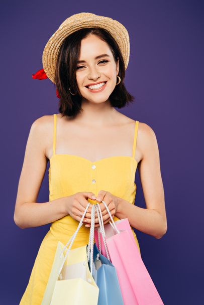 mor izole alışveriş çantaları tutan hasır şapka gülümseyen kız - Fotoğraf, Görsel