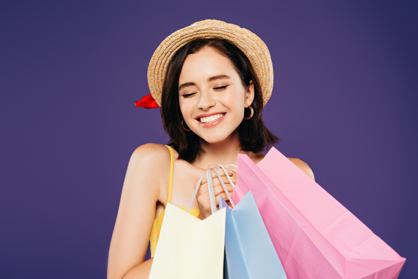 smiling girl in straw hat with closed eyes and shopping bags isolated on purple - Foto, immagini