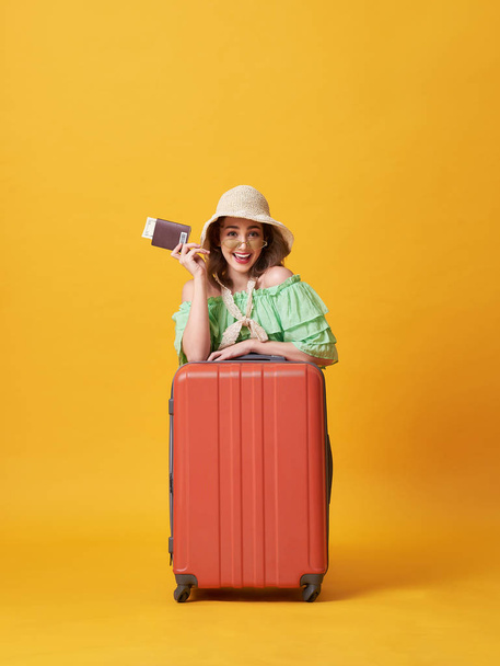 Cheerful young woman dressed in summer clothes holding passport with money while hug with suitcase isolated over yellow background. - Foto, afbeelding