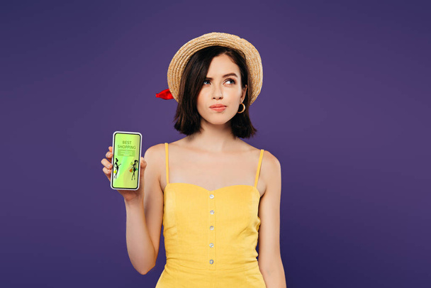 dreamy pretty girl in straw hat holding smartphone with best shopping app isolated on purple  - Fotoğraf, Görsel
