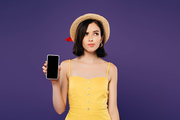 zasněný hezká dívka v slaměném klobouku přidržoval telefon Smartphone s prázdnou obrazovkou izolovanou na purpurové  - Fotografie, Obrázek