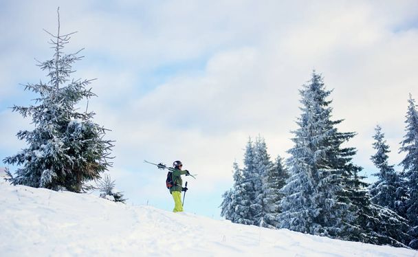Young skier walking down to foothills in mountains with his skis on shoulder after solitary skiing in winter frosty day - Photo, Image