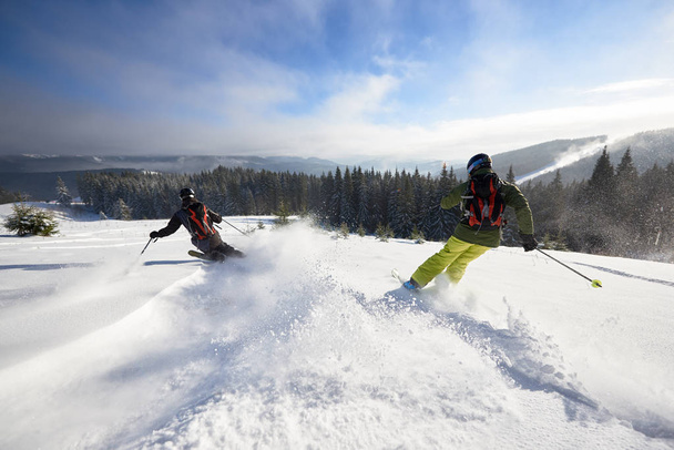 Visão traseira de esquiadores masculinos agressivos fazendo pó de neve profunda enquanto esqui e escultura rápido para baixo na encosta arborizada aberta larga
 - Foto, Imagem