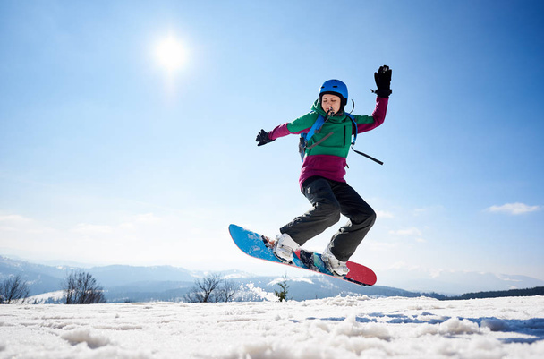junge Snowboarderin reitet Snowboard auf Kopie Weltraum Hintergrund des klaren strahlend blauen Himmels und schneebedeckten Bergen an sonnigen Wintertag - Foto, Bild