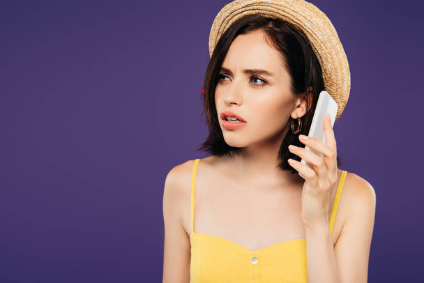 worried pretty girl in straw hat talking on smartphone isolated on purple  - Photo, Image