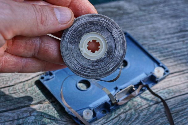 частина старої аудіокасети з коричневою боббіновою плівкою в пальцях
 - Фото, зображення