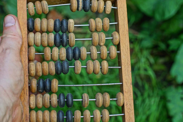 hand houdt oude bruine houten Abacus op een groene achtergrond - Foto, afbeelding