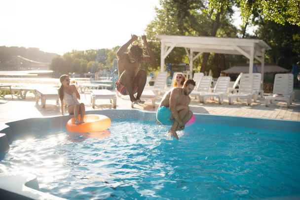 Boyfriends jumping into water while chilling near pool with women - Foto, afbeelding