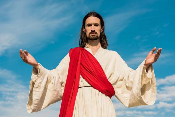 bärtiger Jesus mit ausgestreckten Händen gegen blauen Himmel  - Foto, Bild