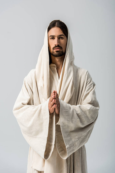 религиозный человек с молящимися руками и в одежде Иисуса с капюшоном, стоящим изолированным на сером
  - Фото, изображение