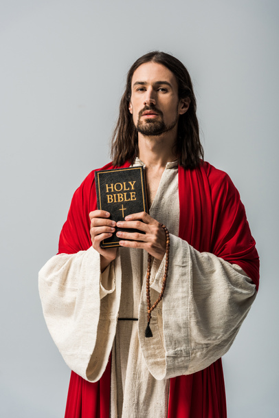 hombre sosteniendo cuentas de rosario y la sagrada Biblia y mirando a la cámara aislada en gris
  - Foto, imagen