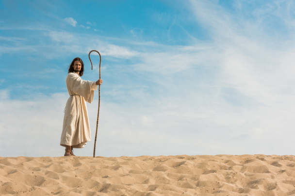 jesus holding wooden cane against blue sky in desert  - Photo, Image