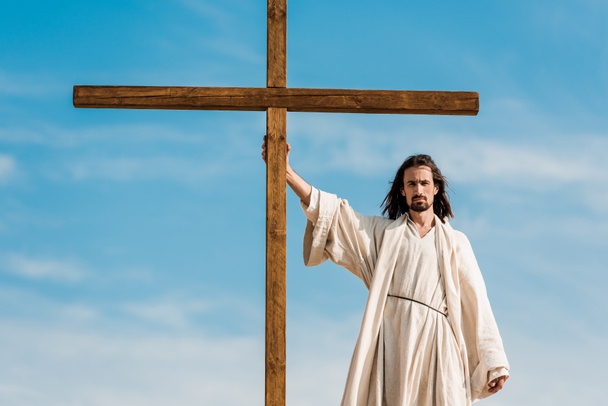 przystojny człowiek stoi i trzyma drewniany krzyż  - Zdjęcie, obraz