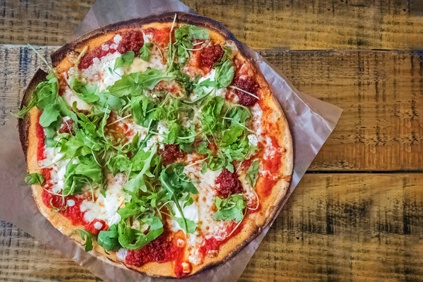 Свіжа запечена піца з тонкою скоринкою, з томатним соусом і руколою на дерев'яному столі
 - Фото, зображення