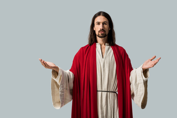religieuze man kijkt naar camera terwijl staande met uitgestrekte handen geïsoleerd op grijs - Foto, afbeelding