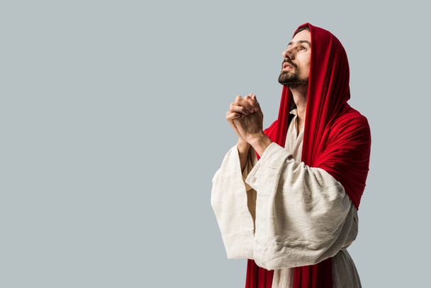 όμορφος άντρας με κόκκινη κουκούλα προσεύχεται απομονωμένος σε γκρι  - Φωτογραφία, εικόνα