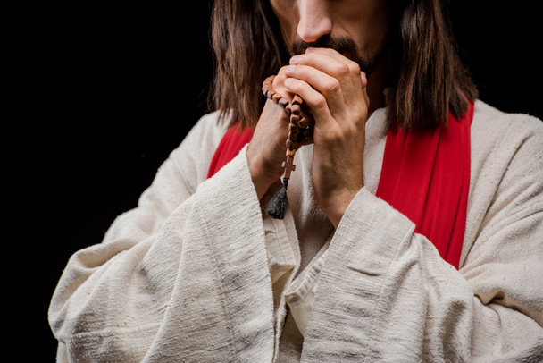 wykadrowany widok człowieka trzymania paciorków różańca podczas modlitwy izolowane na czarnym  - Zdjęcie, obraz