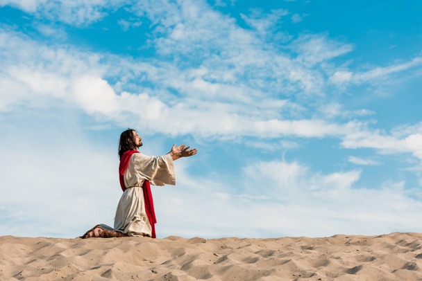 Jesús rezando de rodillas en el desierto contra el cielo
  - Foto, imagen