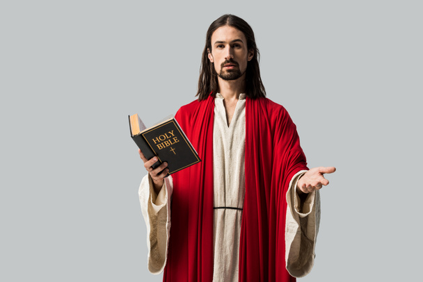 hombre guapo gesticulando y sosteniendo la sagrada Biblia aislada en gris
  - Foto, Imagen