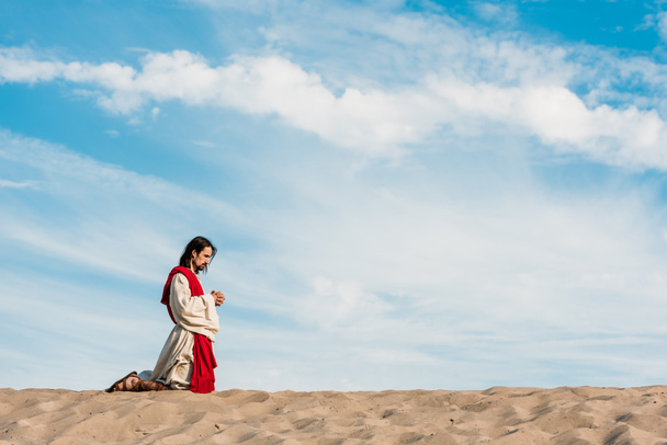 άνθρωπος προσεύχεται στα γόνατα με σφικτά χέρια στην έρημο  - Φωτογραφία, εικόνα