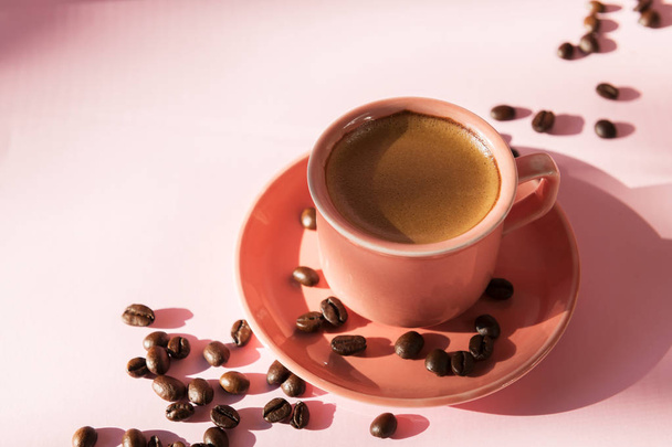 パステルローズの背景に影を持つエッフェスコーヒーの豆とサンゴ色のカップ。平らな横たわる。トップビュー。コーヒーのコンセプト。ポップアート静物 - 写真・画像