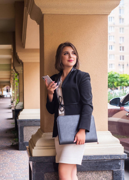 Портрет улыбающейся красивой деловой девушки в городе с телефоном
. - Фото, изображение