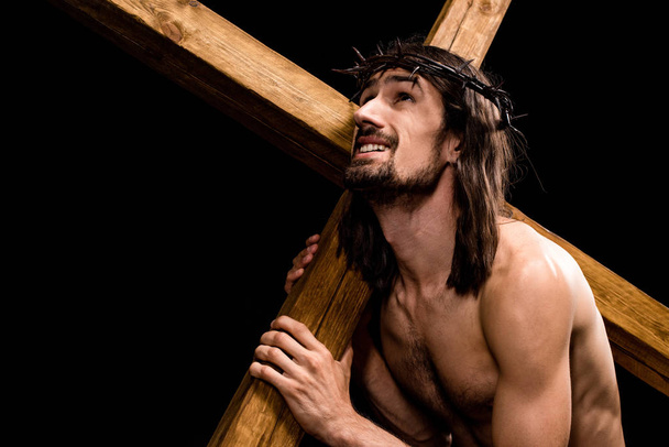 bearded shirtless man in wreath holding cross isolated on black  - Foto, Imagen