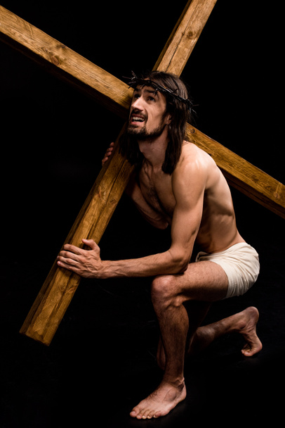 ο Ιησούς κρατώντας βαρύ ξύλινο σταυρό ενώ κάθεται σε μαύρο  - Φωτογραφία, εικόνα